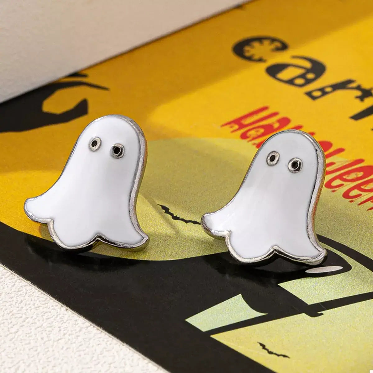 Ghost-shaped earrings on a Halloween-themed background