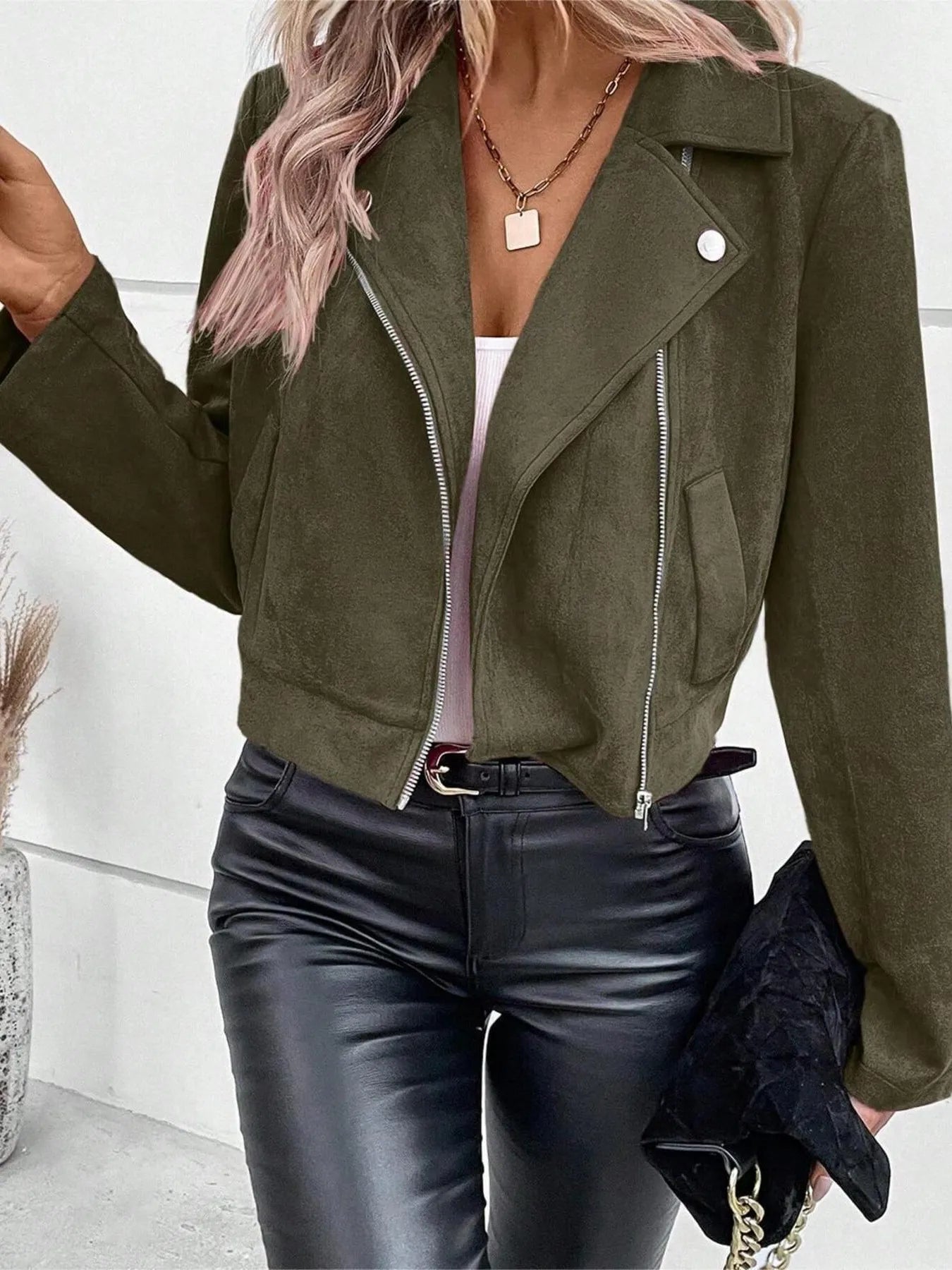 Person wearing a green suede jacket and black leather pants indoors.