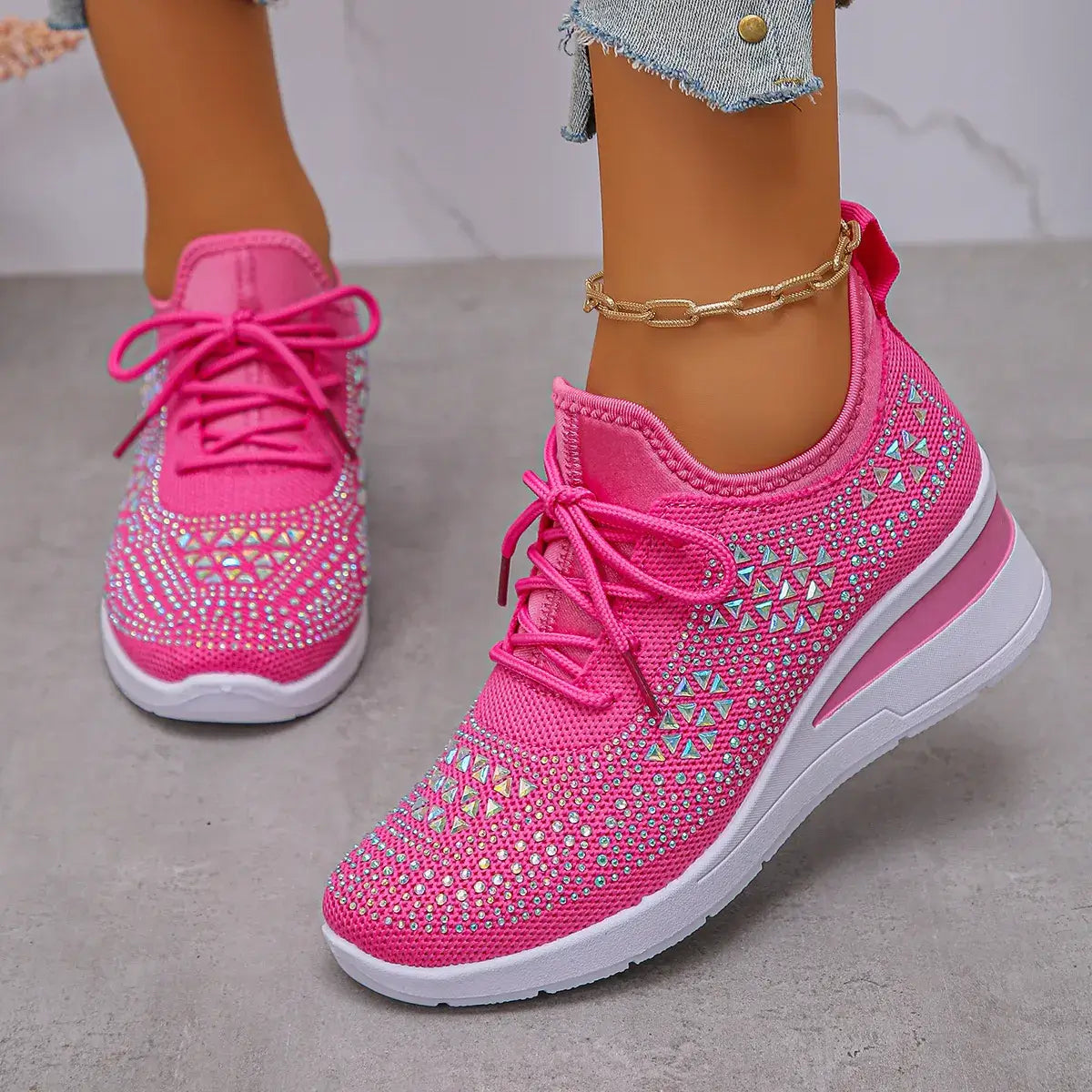Pink sneakers with rhinestone details worn by a person on a neutral background