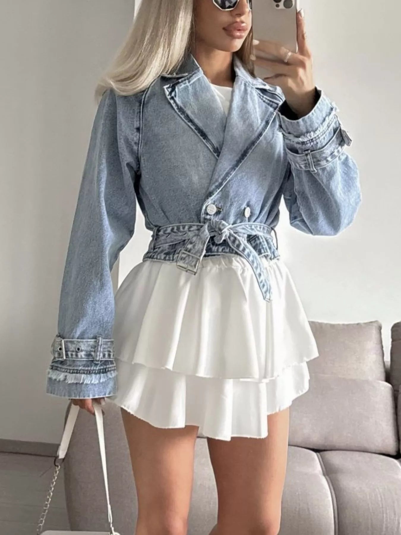 Person wearing a denim jacket and white skirt taking a mirror selfie.