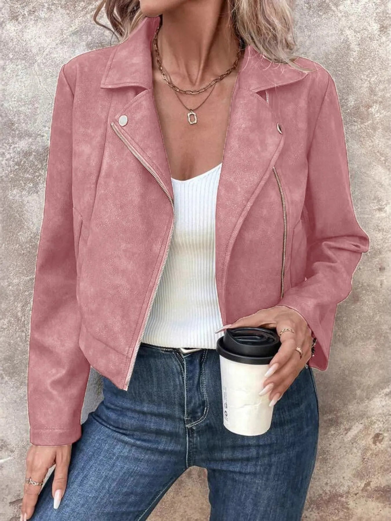 Person wearing a pink suede jacket holding a coffee cup against a neutral background