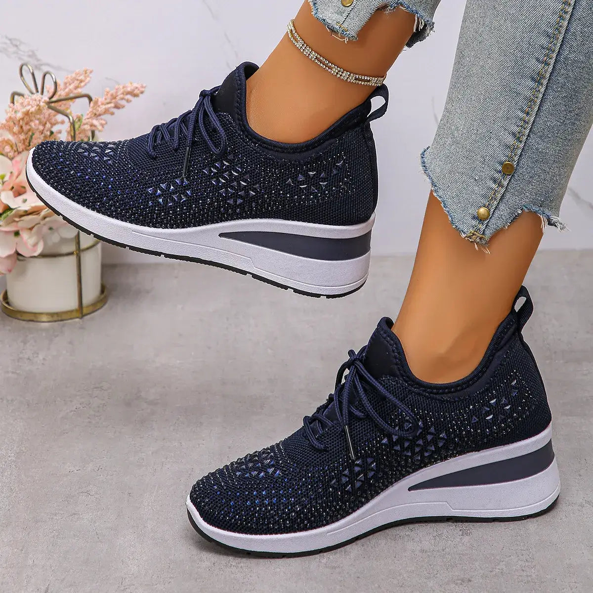 Navy blue sneakers with white soles worn by a person on a light gray surface.