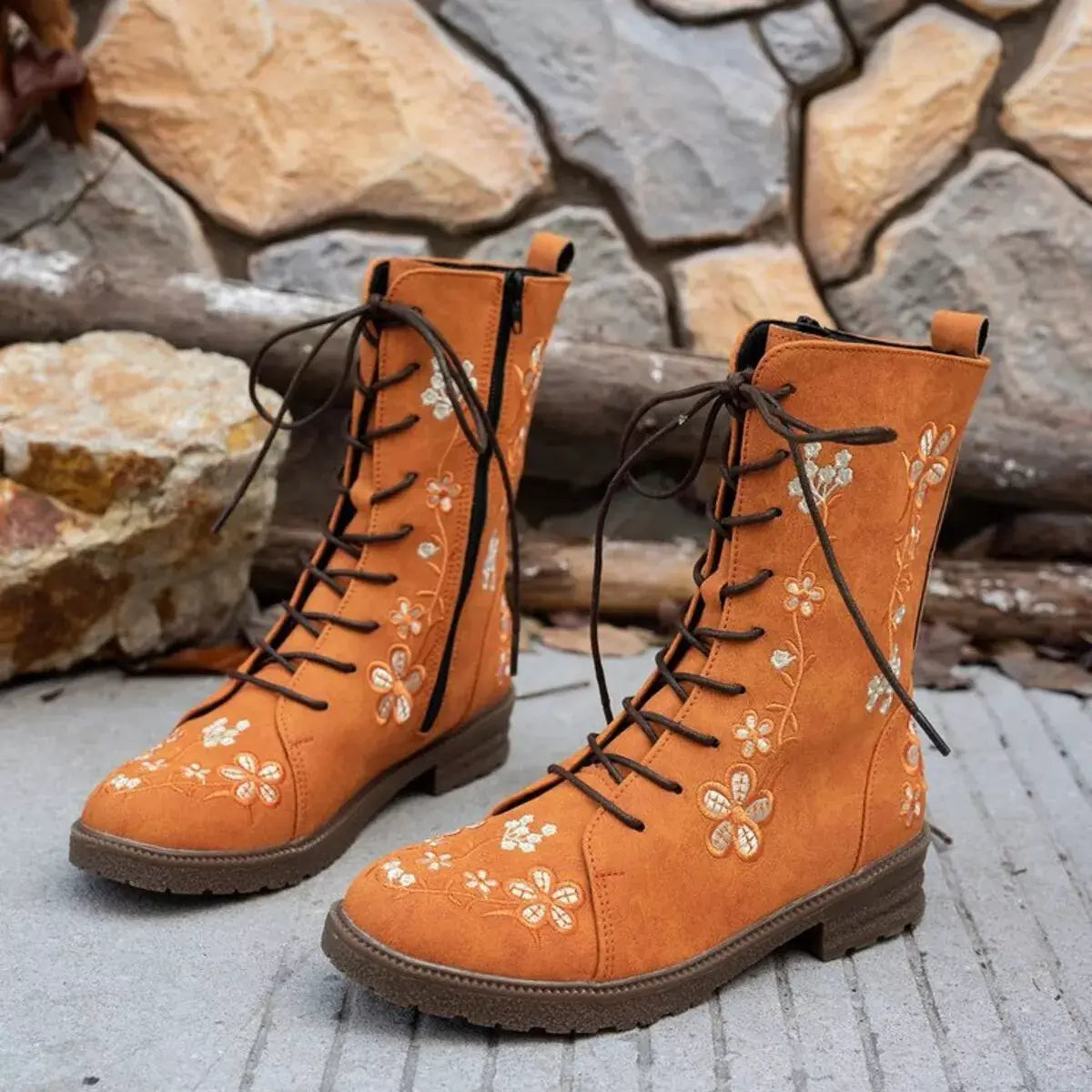 Pair of orange boots with floral embroidery on a stone surface and stone wall background