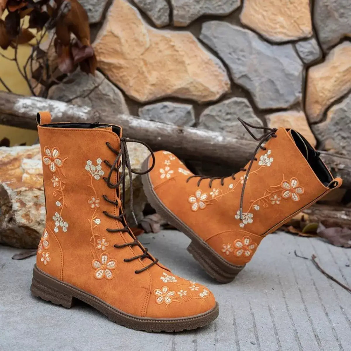 Pair of orange boots with floral embroidery on a stone surface.