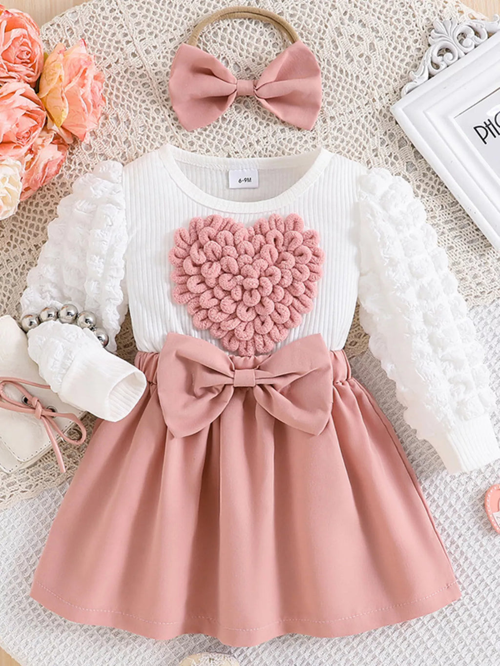 Children's outfit with pink heart-shaped top and skirt on a textured surface.