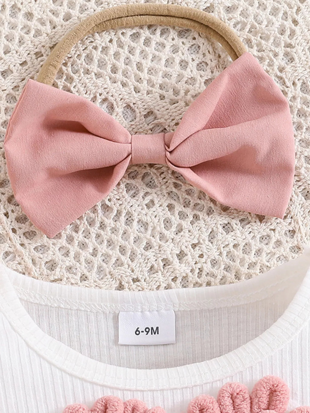 Pink bow headband on a textured surface with a size label