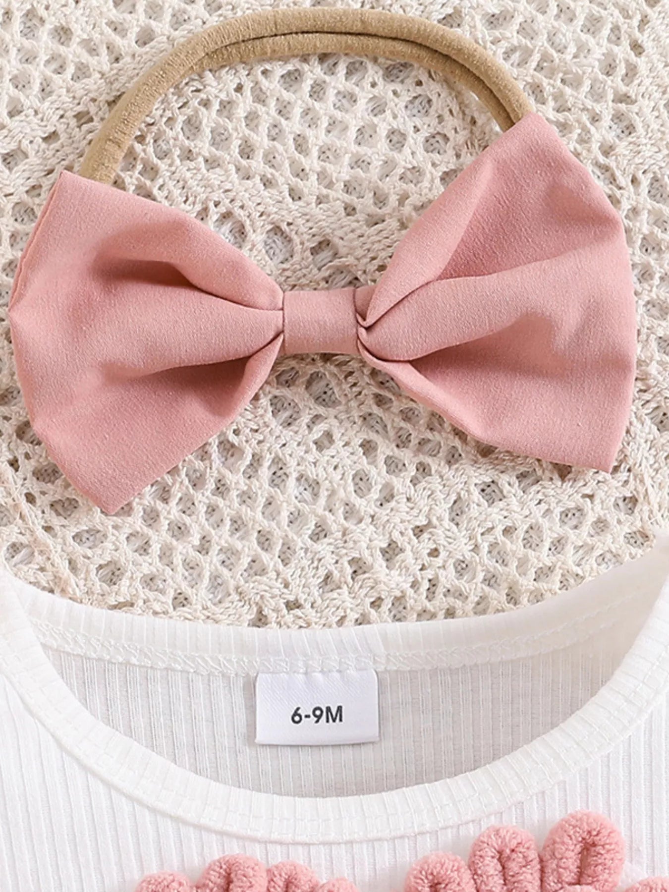 Pink bow headband on a textured surface with a size label
