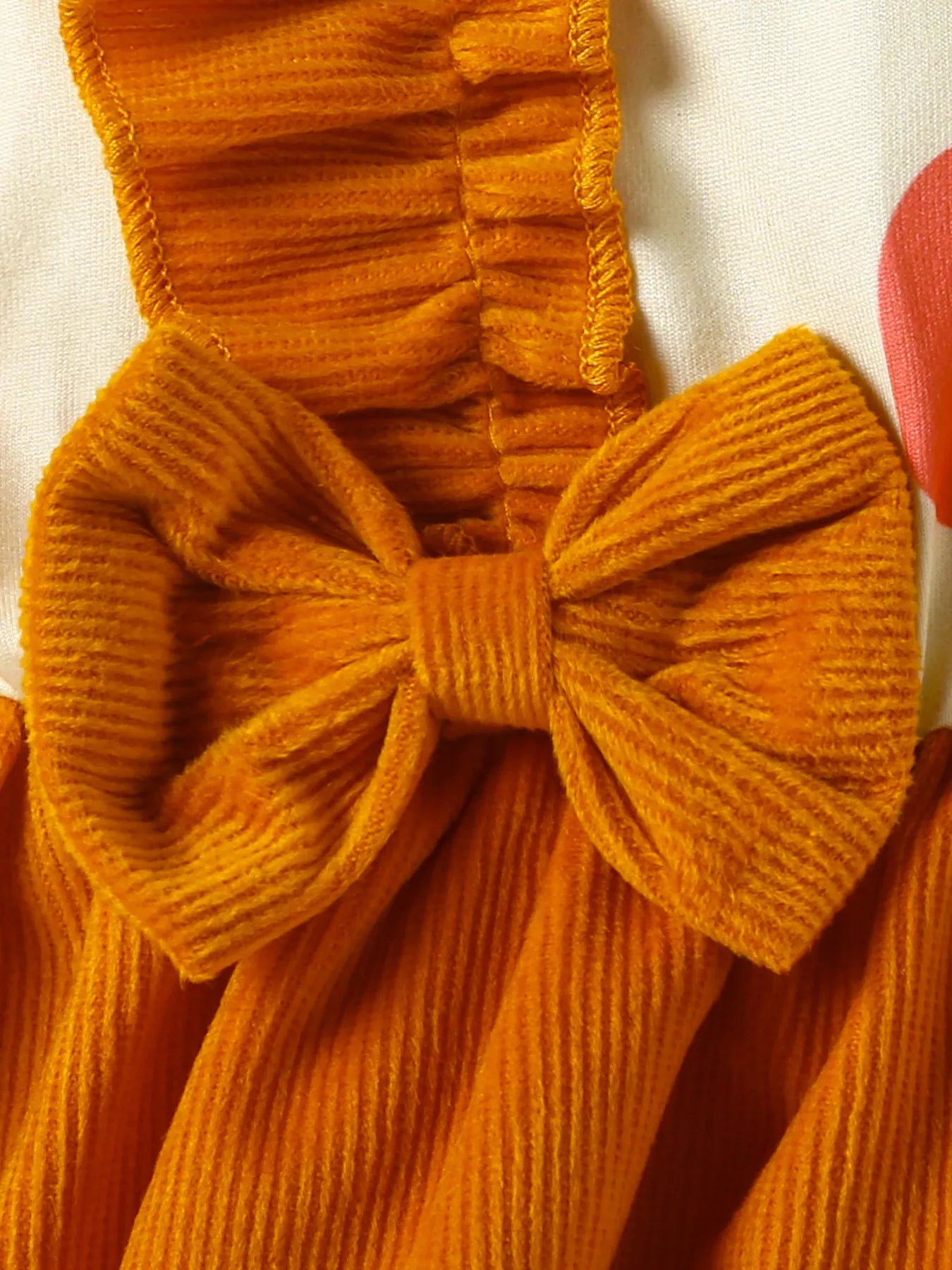 Close-up of an orange textured garment with a bow detail on a white background