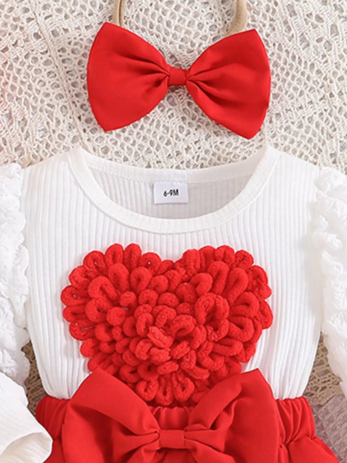 White outfit with red heart design and bow on a textured background