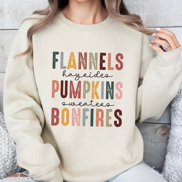 Person wearing a cream sweatshirt with colorful text design on a neutral background