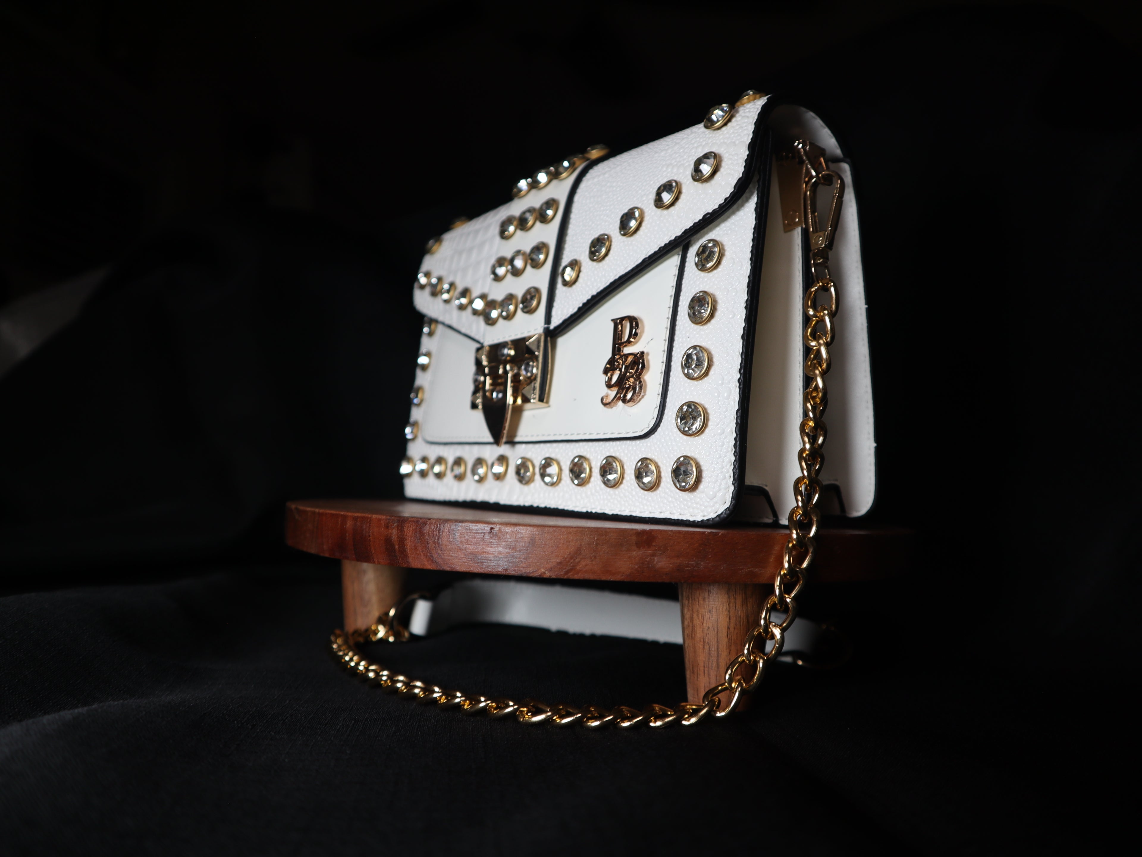White handbag with gold chain and embellishments on a dark background