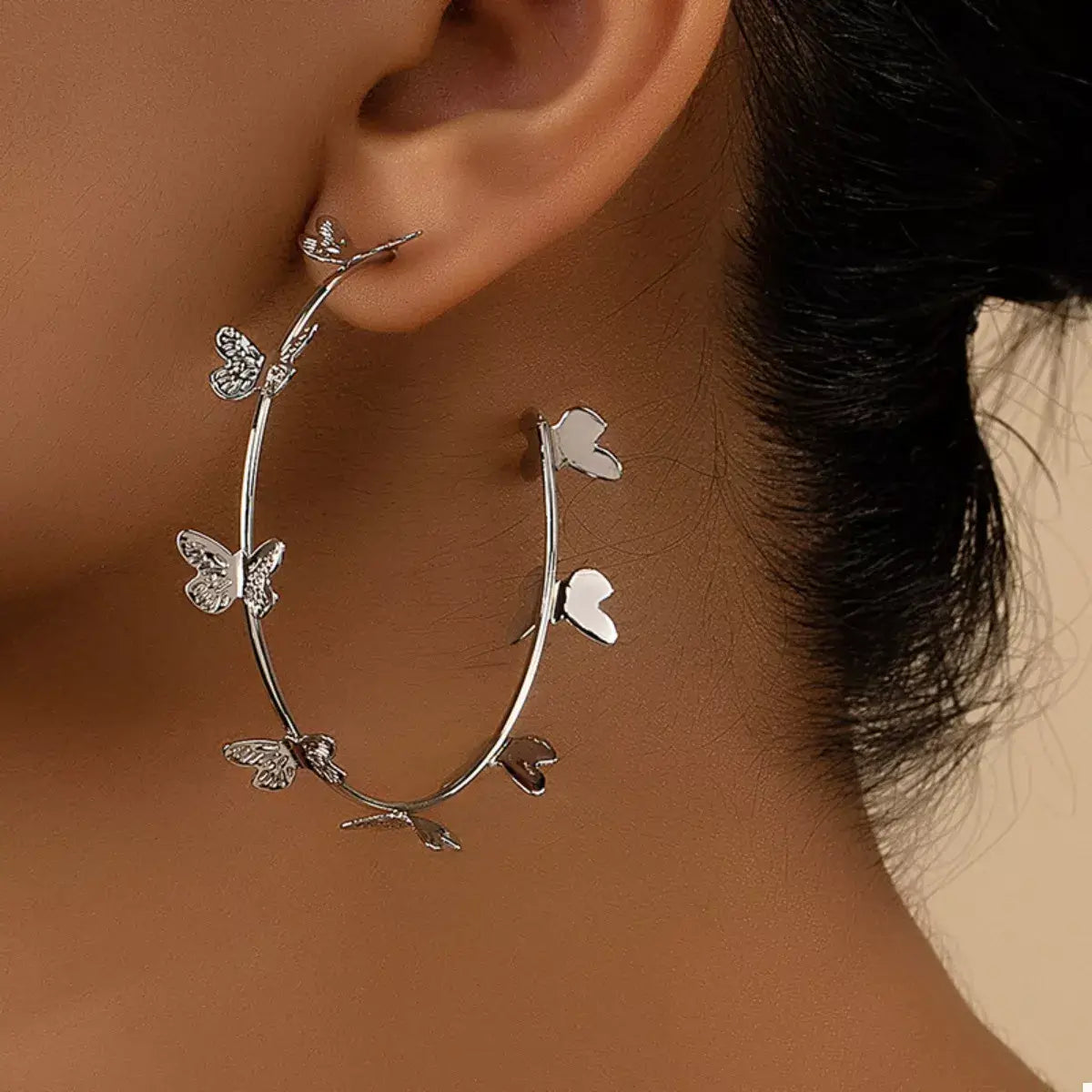 Silver hoop earrings with butterfly and leaf designs worn by a person.