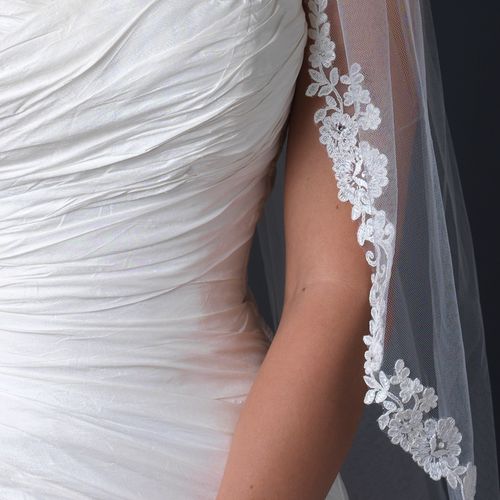 Elegant ivory lace bridal veil with floral embroidery, enhancing a wedding gown for a refined look.