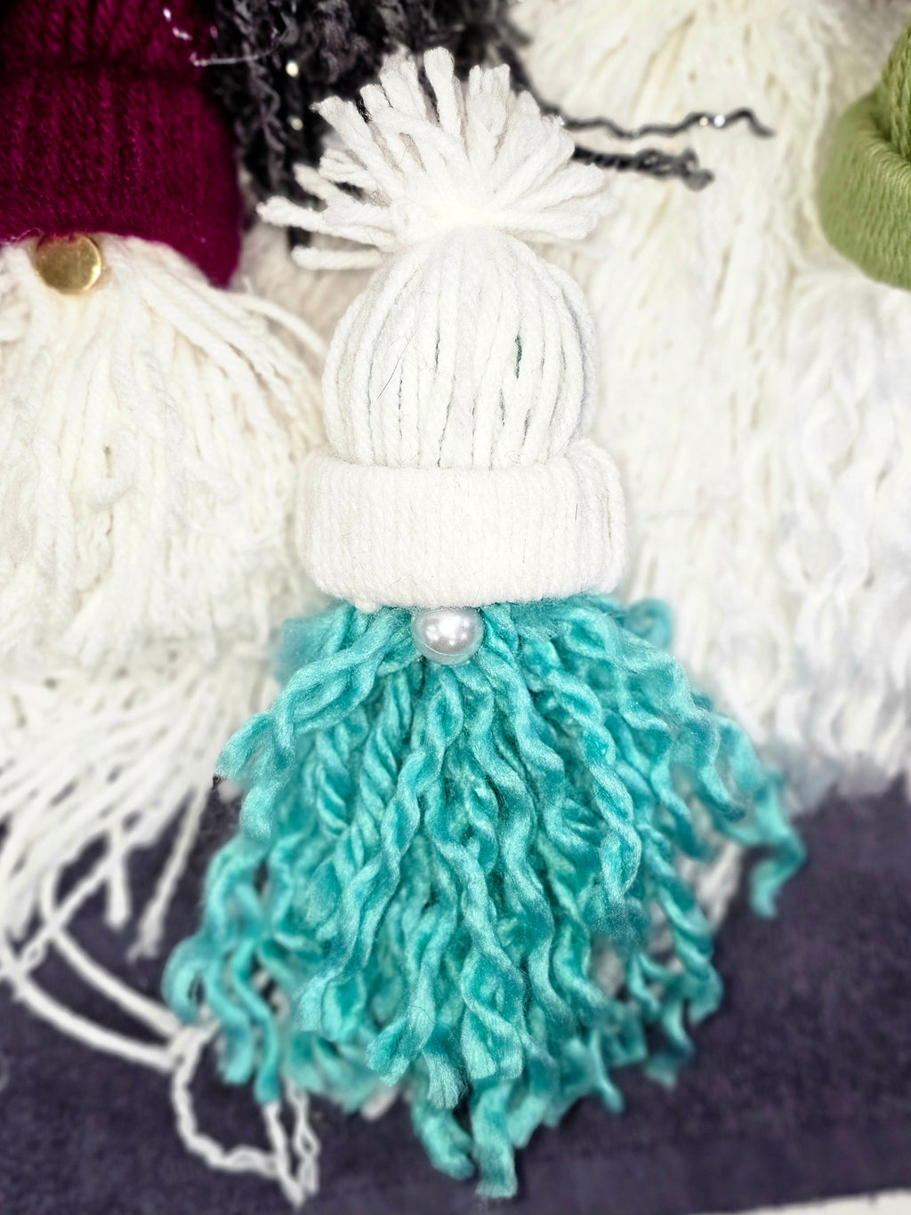 Knitted gnome with white hat and teal pants, surrounded by yarn balls.
