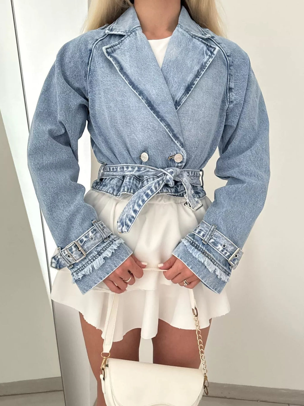 Person wearing a denim jacket over a white dress with a plain background