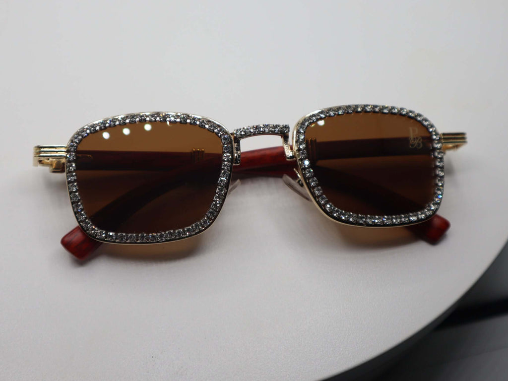 Stylish women's rhinestone sunglasses with brown lenses and gold detailing on a round display.