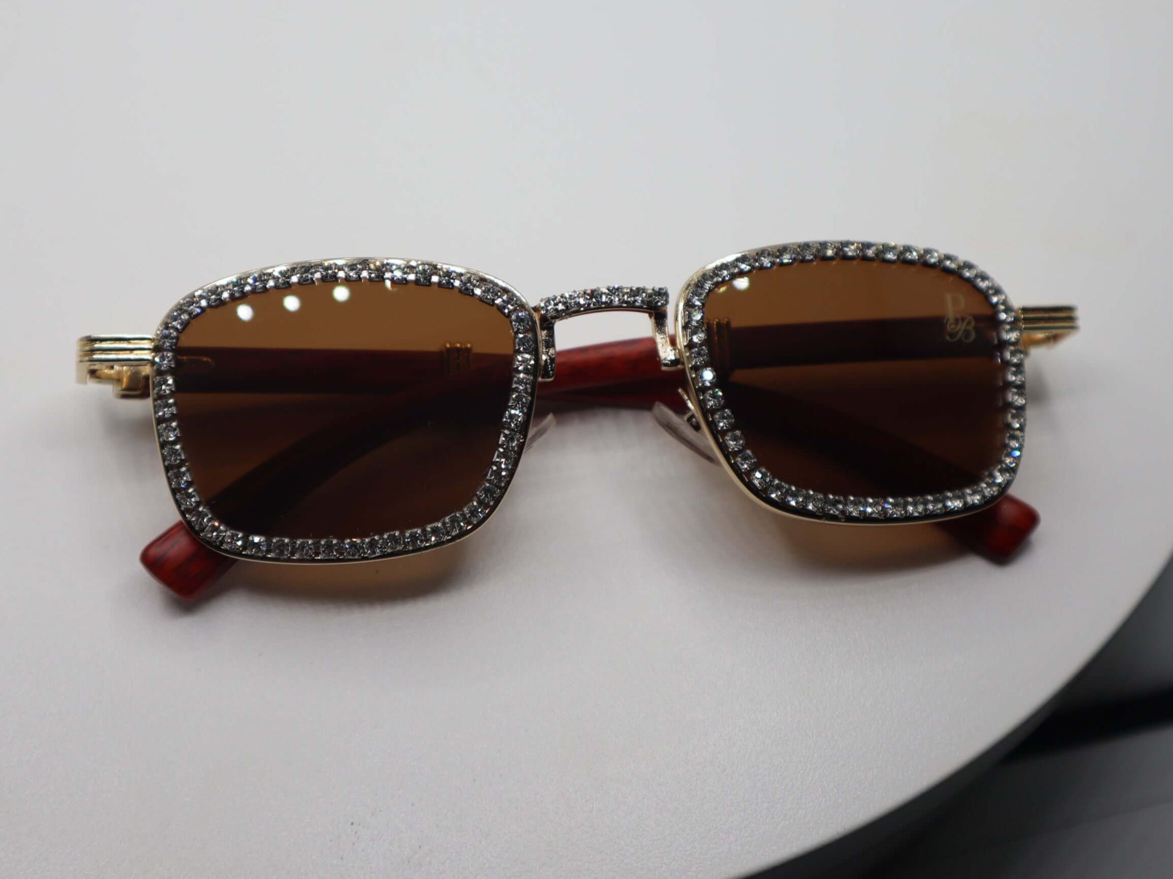 Stylish women's rhinestone sunglasses with brown lenses and gold detailing on a round display.